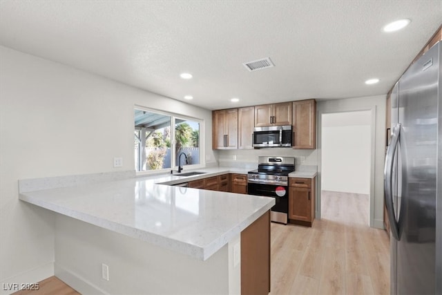 kitchen with visible vents, a sink, stainless steel appliances, light wood-style floors, and a peninsula