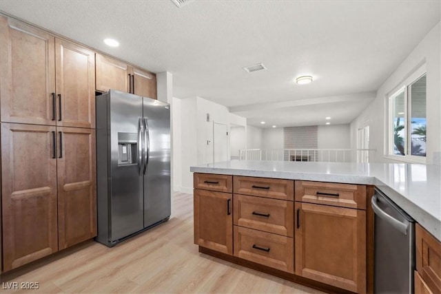 kitchen with visible vents, light wood-type flooring, light countertops, a peninsula, and stainless steel appliances