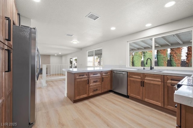 kitchen with visible vents, brown cabinets, a sink, stainless steel appliances, and a peninsula