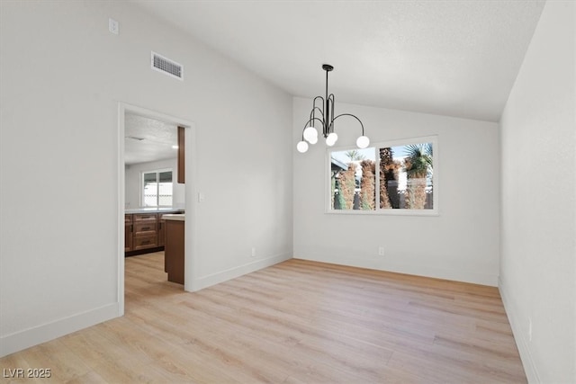 spare room featuring visible vents, a notable chandelier, light wood-style floors, baseboards, and vaulted ceiling