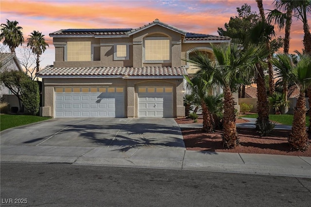 view of front of home featuring stucco siding, driveway, a tile roof, a garage, and solar panels