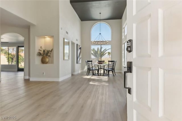 foyer with baseboards, light wood-type flooring, arched walkways, and an inviting chandelier