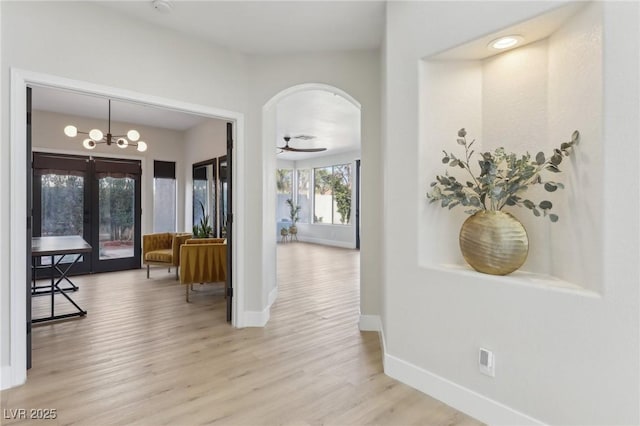 corridor featuring baseboards, light wood-style floors, a chandelier, and arched walkways