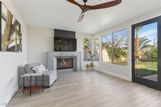 sitting room featuring a glass covered fireplace, baseboards, wood finished floors, and a ceiling fan