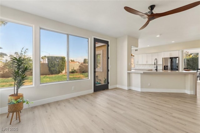 unfurnished living room with ceiling fan, baseboards, recessed lighting, light wood-style floors, and a sink