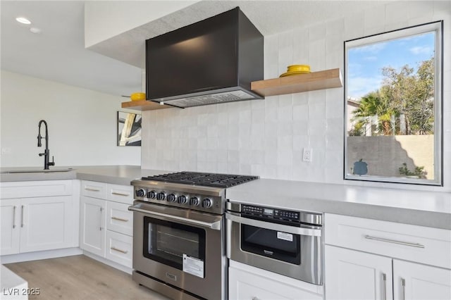 kitchen featuring open shelves, wall chimney range hood, decorative backsplash, stainless steel range, and a sink