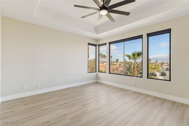 empty room with light wood-style flooring, baseboards, a tray ceiling, and a ceiling fan