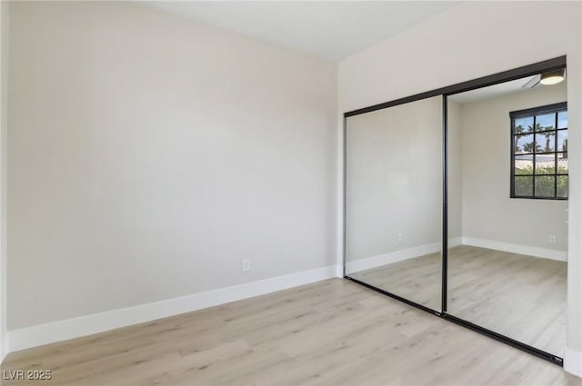 unfurnished bedroom featuring light wood-type flooring, baseboards, and a closet