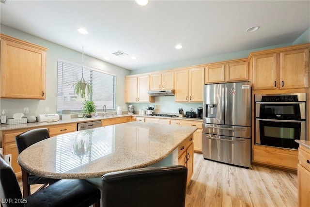 kitchen featuring visible vents, light brown cabinetry, a kitchen breakfast bar, stainless steel appliances, and a sink