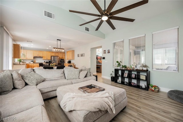 living area featuring visible vents, baseboards, light wood-style floors, and vaulted ceiling