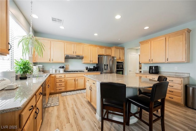 kitchen featuring light brown cabinetry, under cabinet range hood, a center island, appliances with stainless steel finishes, and a breakfast bar area