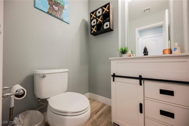 bathroom with visible vents, toilet, wood finished floors, baseboards, and vanity