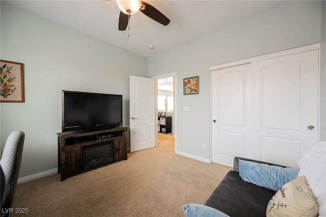 living area featuring light carpet, a ceiling fan, and baseboards