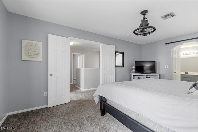 carpeted bedroom with arched walkways, visible vents, ensuite bath, and baseboards