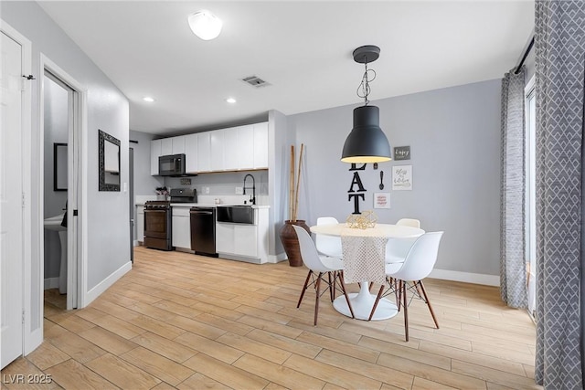 kitchen with visible vents, black appliances, white cabinets, light countertops, and light wood-style floors