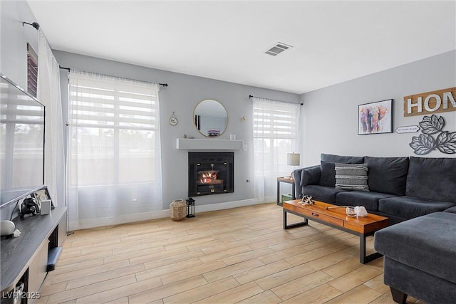 living area with visible vents, baseboards, light wood-style floors, and a glass covered fireplace