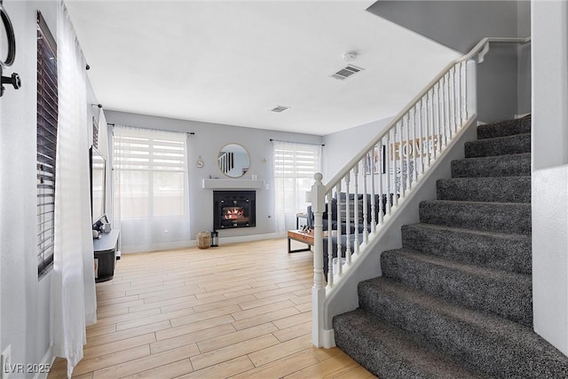 stairway featuring wood finished floors, visible vents, a warm lit fireplace, and baseboards