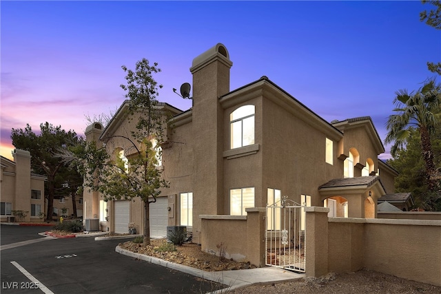 view of side of property with a fenced front yard, central air condition unit, stucco siding, a chimney, and a gate