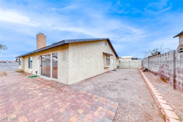 back of house featuring a patio area, stucco siding, a fenced backyard, and a chimney