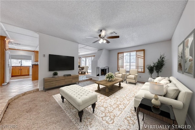 living area featuring light tile patterned floors, visible vents, ceiling fan, a textured ceiling, and a large fireplace