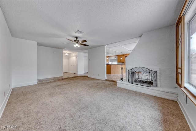 unfurnished living room with visible vents, a textured ceiling, carpet floors, a brick fireplace, and ceiling fan