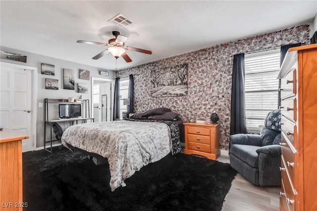 bedroom featuring visible vents, wood finished floors, wallpapered walls, baseboards, and ceiling fan