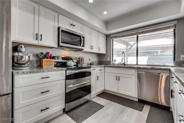 kitchen featuring light wood finished floors, light stone counters, appliances with stainless steel finishes, white cabinets, and a sink