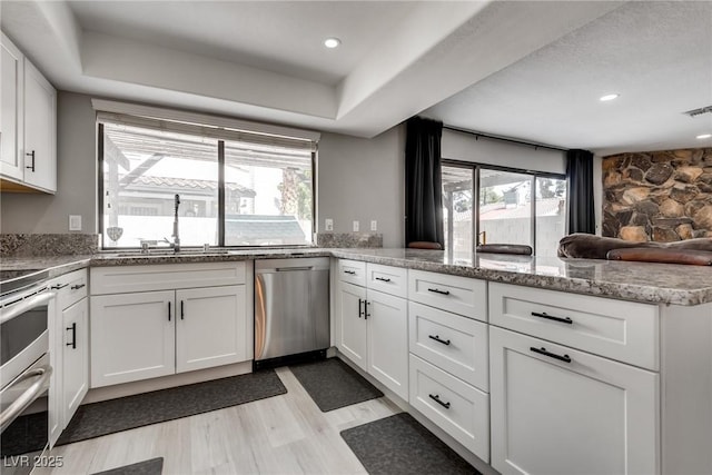 kitchen featuring light wood-type flooring, a peninsula, white cabinets, stainless steel appliances, and a sink