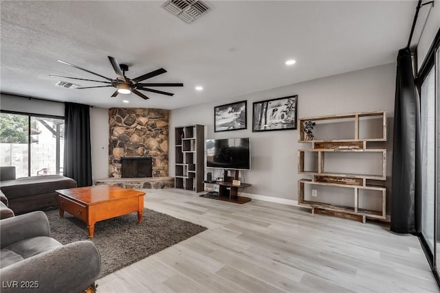 living area with visible vents, wood finished floors, a fireplace, baseboards, and ceiling fan