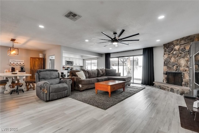 living room featuring visible vents, ceiling fan, a stone fireplace, and light wood-style floors