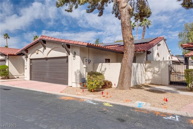 mediterranean / spanish-style home with a tiled roof, fence, roof mounted solar panels, and stucco siding