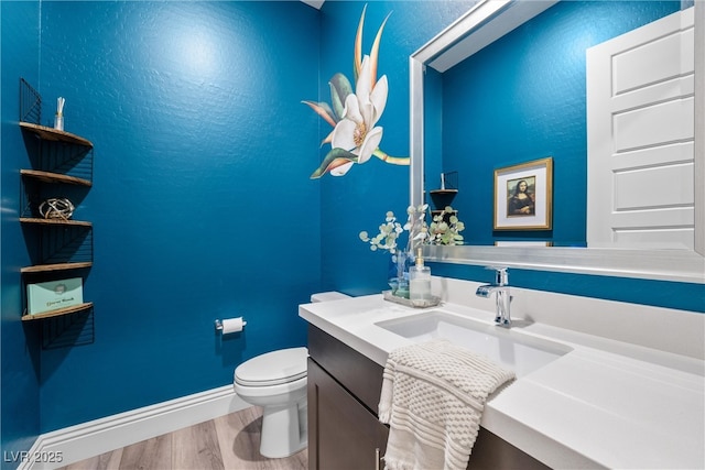 half bath featuring vanity, toilet, wood finished floors, and baseboards