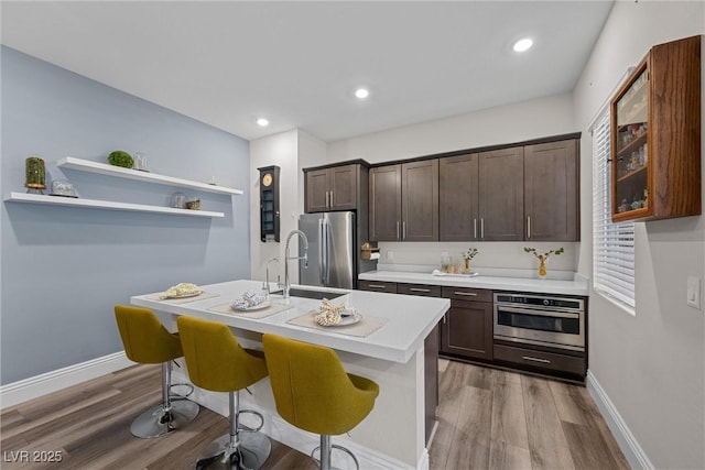 kitchen with light wood-type flooring, a sink, stainless steel appliances, light countertops, and dark brown cabinets