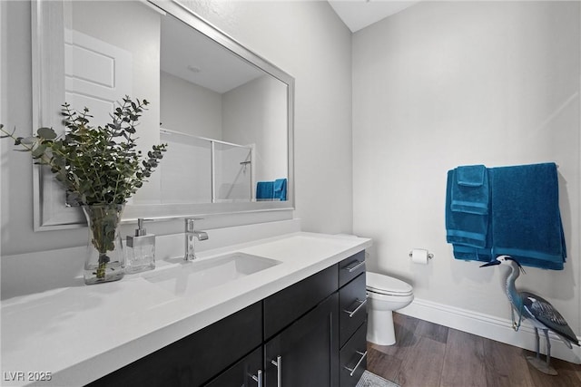 bathroom with vanity, wood finished floors, baseboards, walk in shower, and toilet