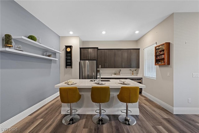 kitchen featuring dark brown cabinetry, freestanding refrigerator, baseboards, and a sink