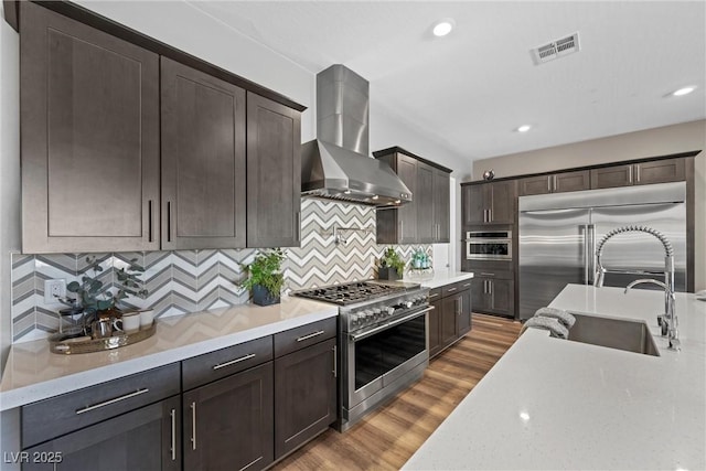 kitchen with wood finished floors, visible vents, high quality appliances, dark brown cabinets, and wall chimney exhaust hood