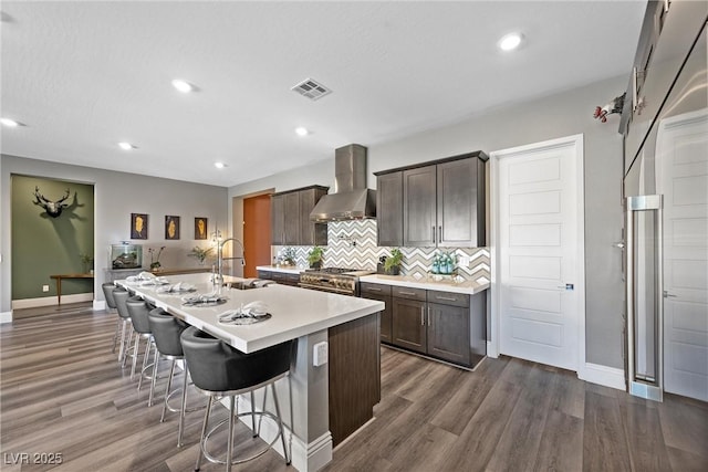 kitchen with visible vents, high end stove, wall chimney range hood, a breakfast bar, and a sink