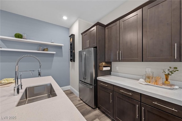 kitchen featuring a sink, open shelves, freestanding refrigerator, dark brown cabinetry, and light countertops