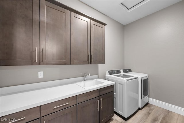 clothes washing area featuring baseboards, washing machine and dryer, light wood-style floors, cabinet space, and a sink