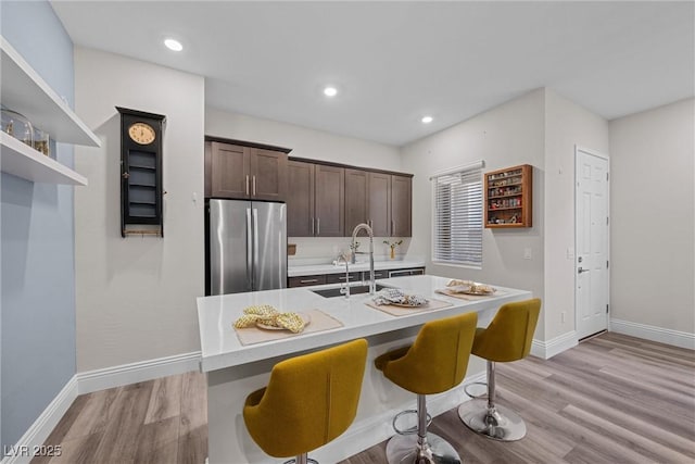 kitchen featuring dark brown cabinets, light wood-type flooring, freestanding refrigerator, and a sink