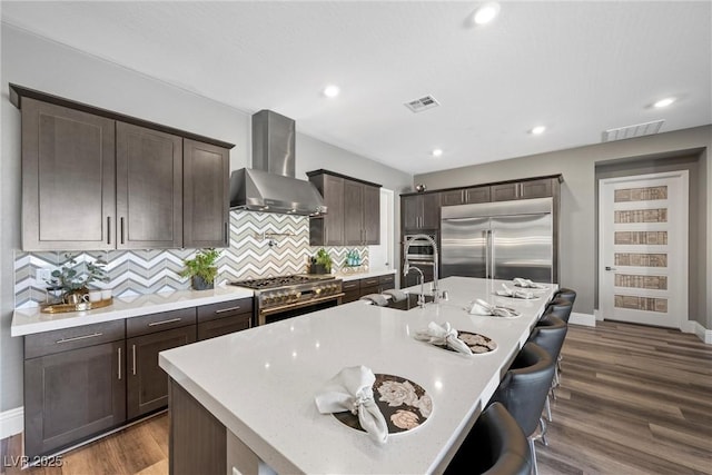 kitchen featuring a sink, visible vents, high end appliances, and wall chimney exhaust hood