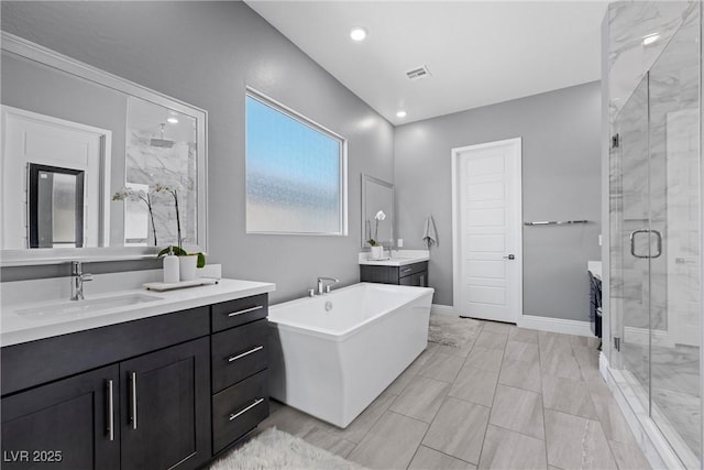 full bath featuring visible vents, a freestanding bath, two vanities, a stall shower, and a sink