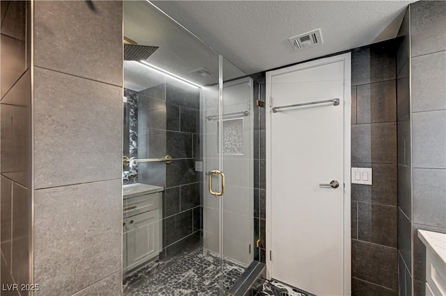 205 E Harmon Ave Unit 1010, Las Vegas, NV 89169 - bathroom featuring a textured ceiling, vanity, visible vents, tile walls, and a stall shower