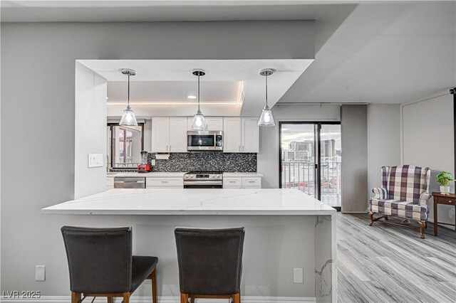 205 E Harmon Ave Unit 1010, Las Vegas, NV 89169 - kitchen with white cabinets, appliances with stainless steel finishes, light wood-style floors, a tray ceiling, and backsplash
