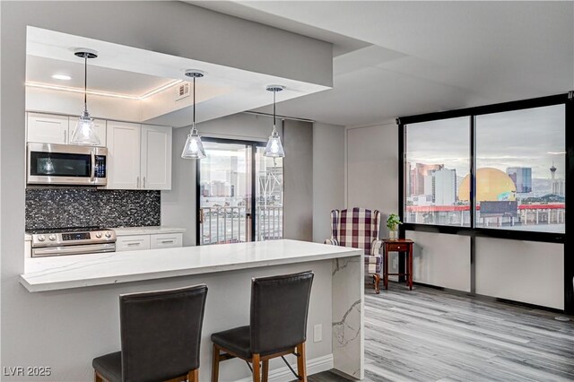 205 E Harmon Ave Unit 1010, Las Vegas, NV 89169 - kitchen featuring light wood-style flooring, white cabinets, a breakfast bar, appliances with stainless steel finishes, and hanging light fixtures
