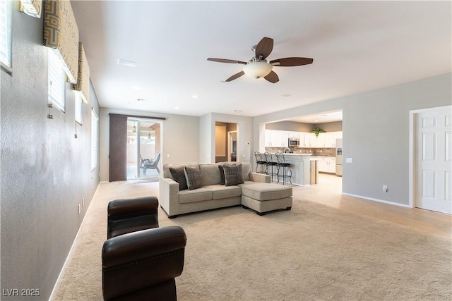 living room with baseboards, light carpet, and a ceiling fan