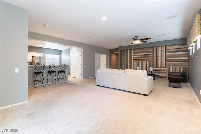 living area featuring visible vents, light colored carpet, baseboards, and ceiling fan