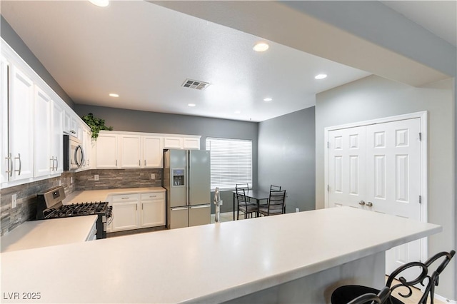 kitchen with visible vents, backsplash, stainless steel appliances, a breakfast bar area, and light countertops