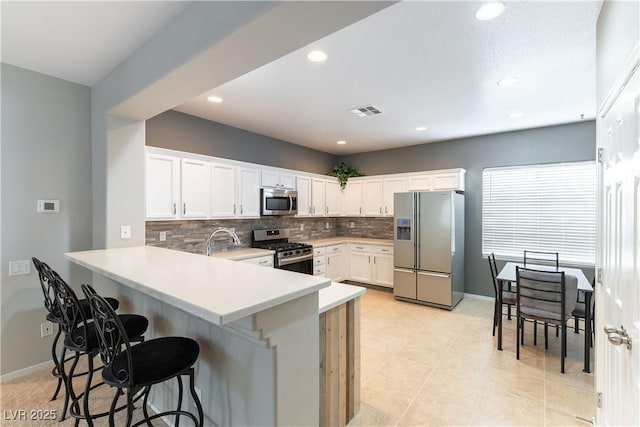 kitchen featuring visible vents, a breakfast bar, tasteful backsplash, stainless steel appliances, and a peninsula