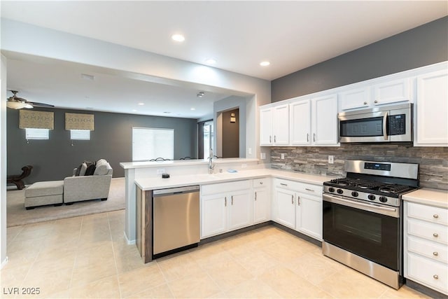 kitchen with a sink, tasteful backsplash, open floor plan, appliances with stainless steel finishes, and white cabinets